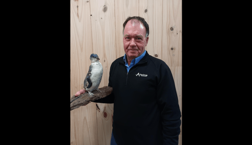 an old white man smiling while holding a very small penguin